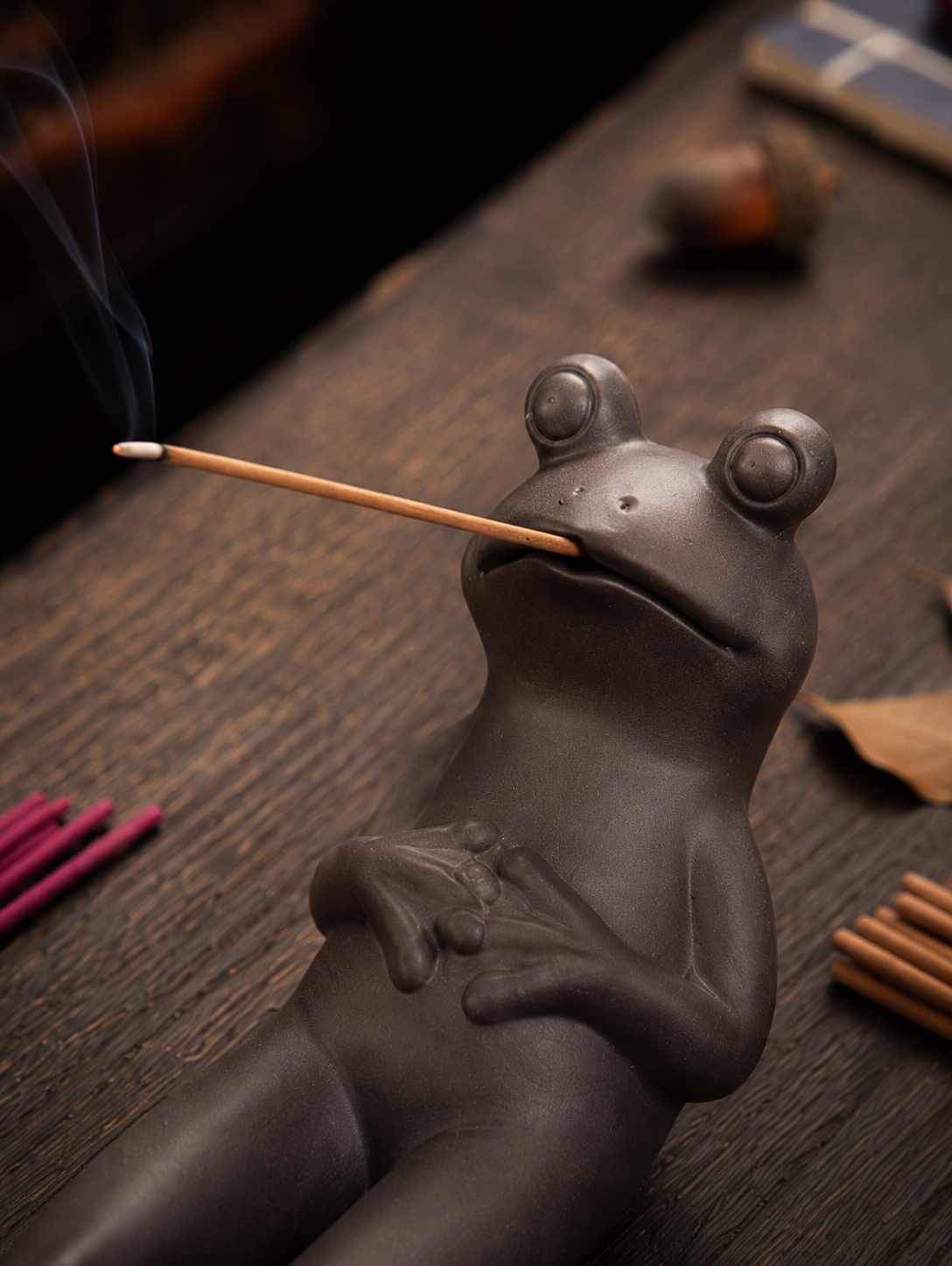 Incensário em argila roxa com sapo relaxando segurando incenso de vareta.