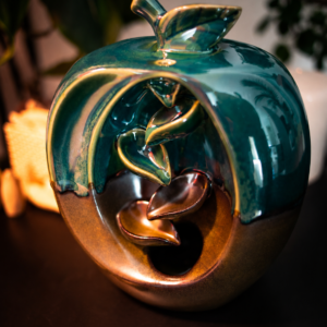 Incensário cascata decorativo em formato de maçã produzido em cerâmica com efeito visual de fumaça descendente.